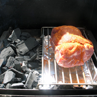 Pork shoulder roast set up on the slow cook rack with drip pan and slow-burn charcoal train